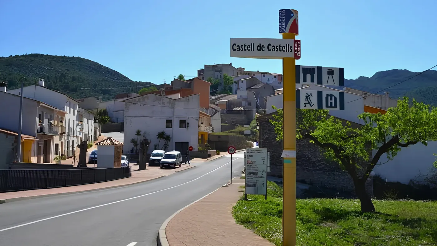 The road into Castell de Castells, the village sign and the mountains behind