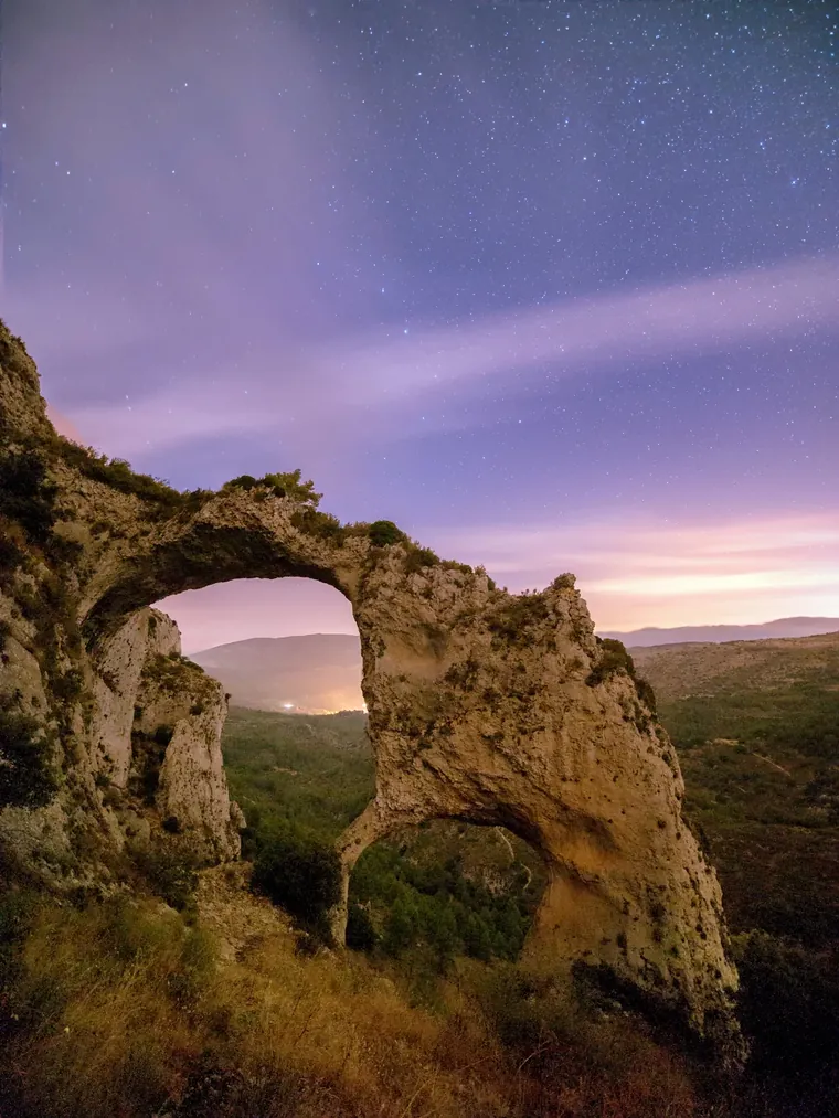 The Els Arcs stone arches at night under a sky full of stars, the village lights below