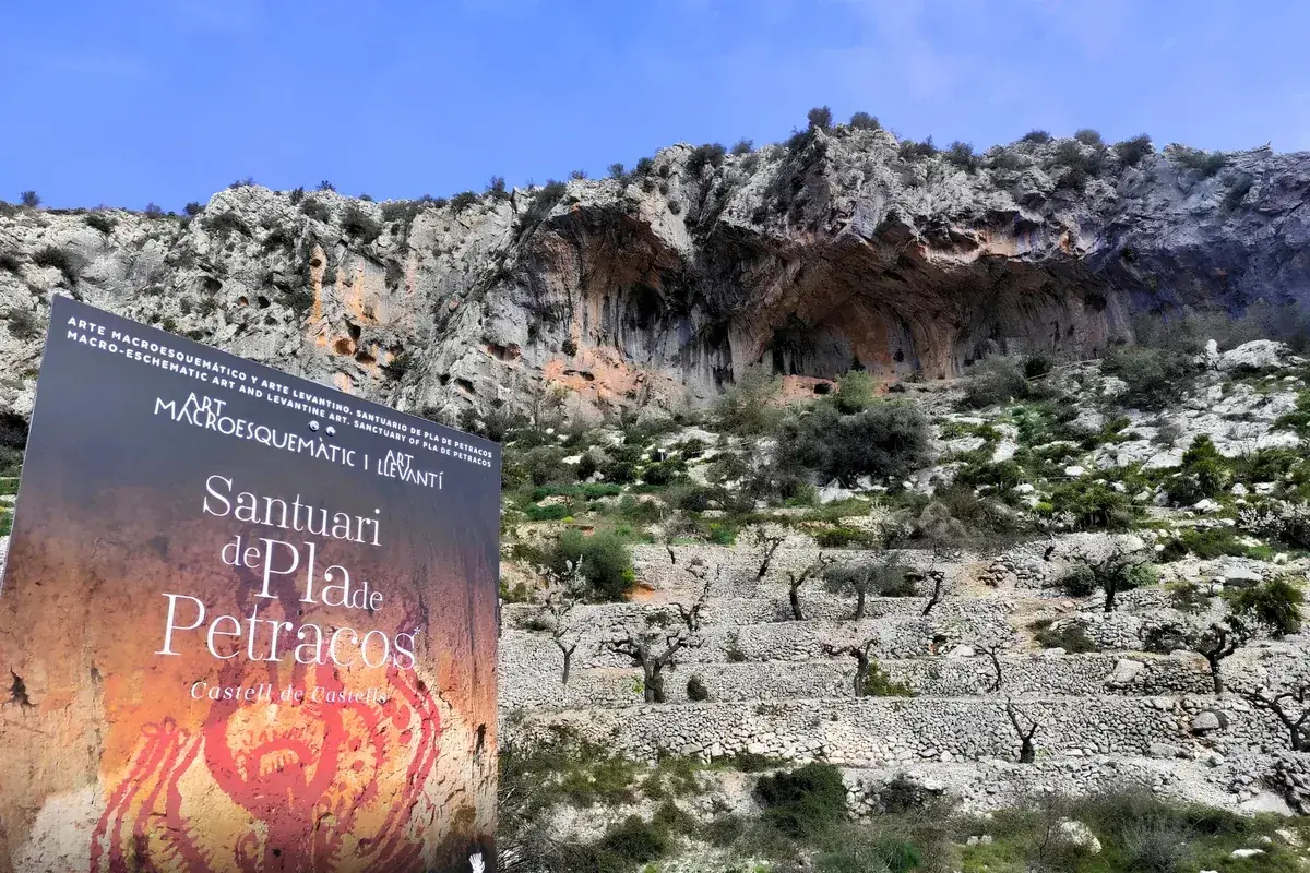 The Santuari de Pla de Petracos sign beneath the rock shelters and almond terraces